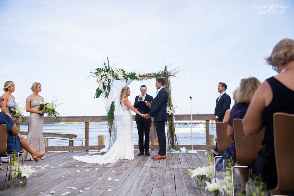 bride and groom getting married under floral arch on dock overlooking water at brannon center florida