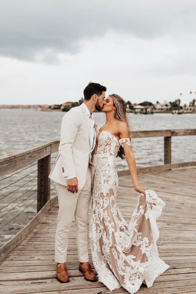 newlywed bride and groom kissing on dock overlooking water outside brannon center florida with clouds rolling in