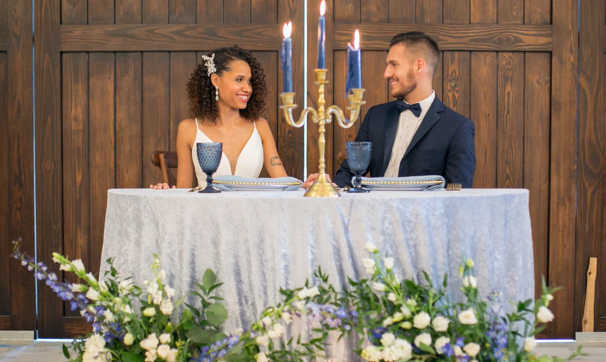 bride and groom seated at sweetheart table with blue linens and matching blue candles