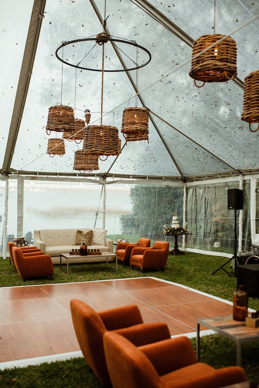 couches tables and chairs setup in outdoor tent for wedding reception with dancefloor and wicker chandeliers