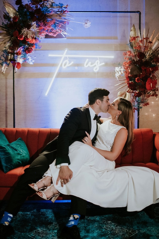 bride and groom kissing on a red couch with matching flowers and a neon 