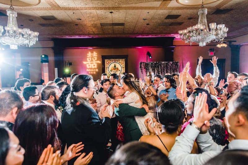 bride and groom kissing on middle of dance floor surrounded by their guests