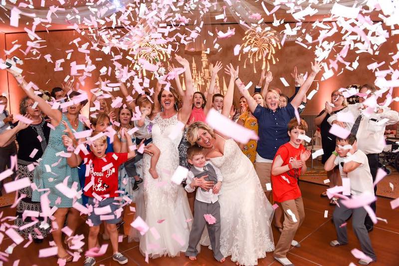 bride and guests cheering while standing on dance floor with confetti falling around them