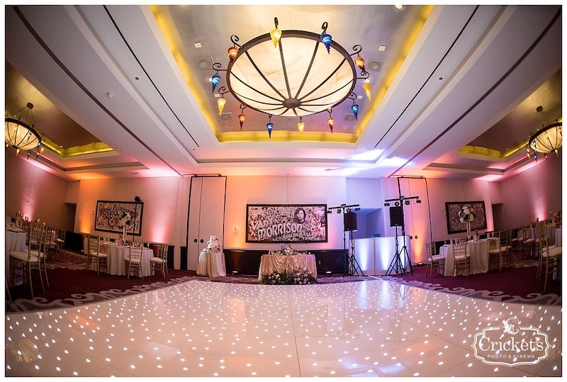 dance floor setup for wedding reception with dj booth in corner and uplights throughout the room