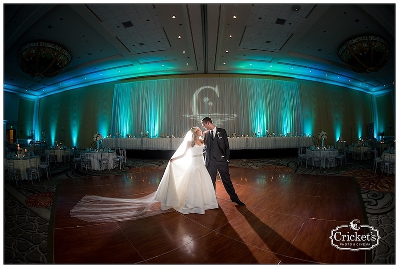 bride and groom embracing while standing in the middle of a dance floor and wall behind them lit up with uplights and gobo