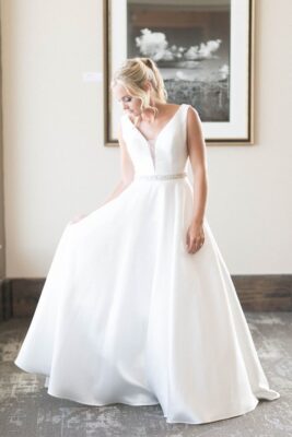 bride looking down at her dress after getting ready for wedding, standing in front of a black and white photo on the wall