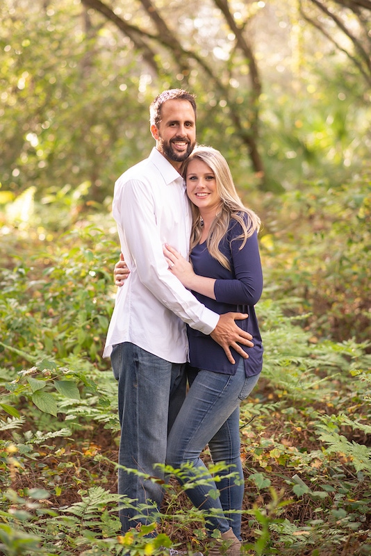 couple embracing while standing in wooded area photo by Cona Studios