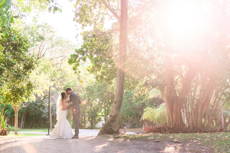 bride and groom kissing while on path near large trees photo by Cona Studios