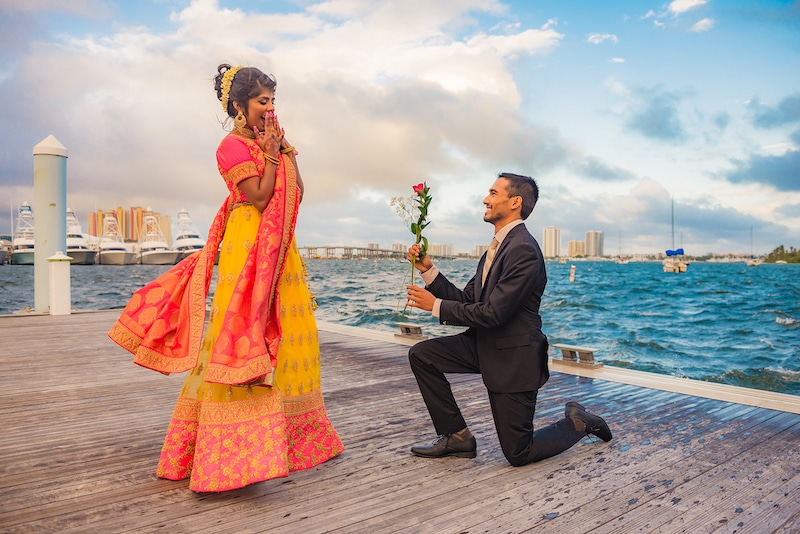 man on one knee offering rose to his bride to be