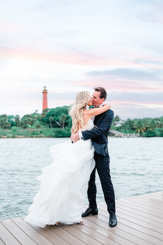 bride and groom kissing on dock with jupiter lighthouse behind them photo by Cona Studios