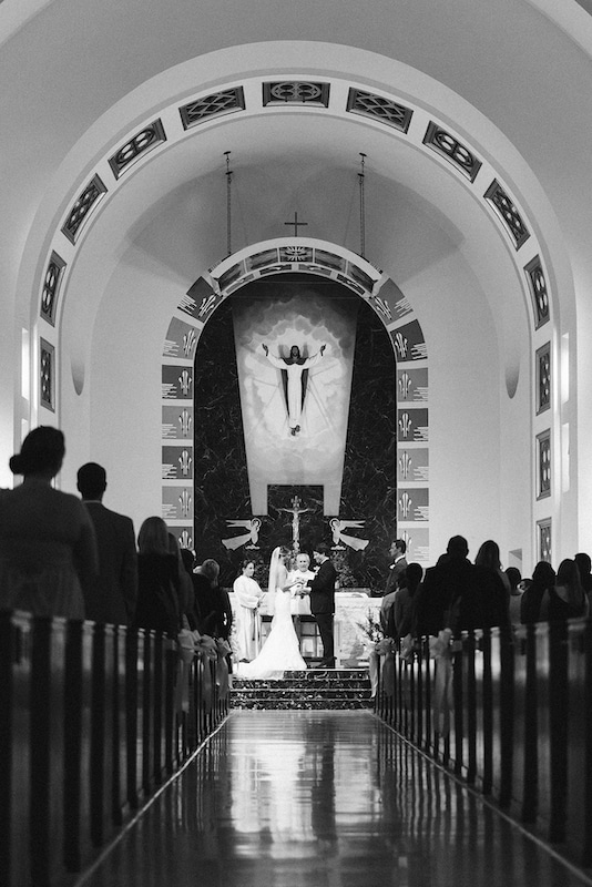 bride and groom getting married inside of church while guests and family watch photo by Cona Studios
