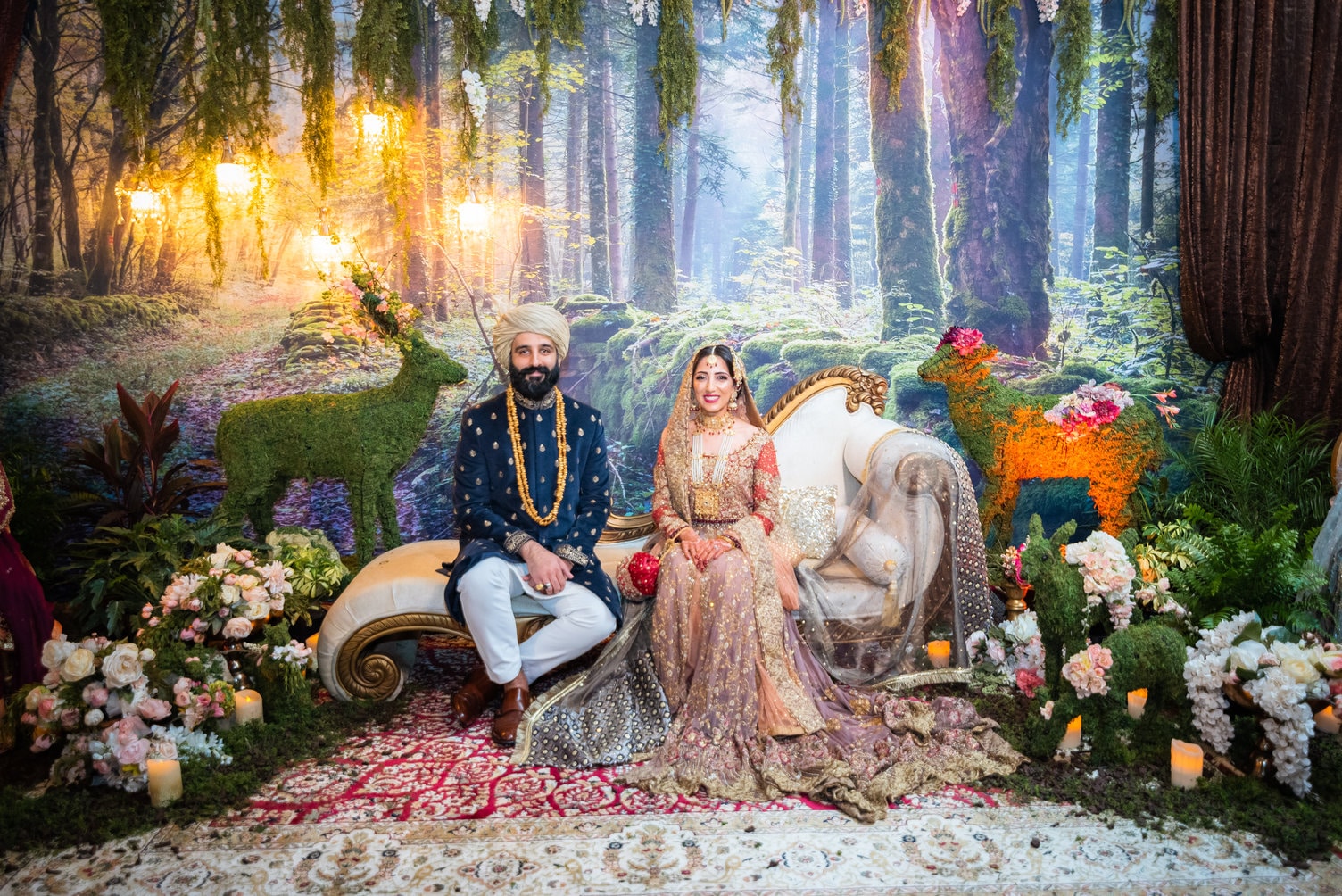 bride and groom sitting on lounge in front of painted landscape detailing an enchanted forest