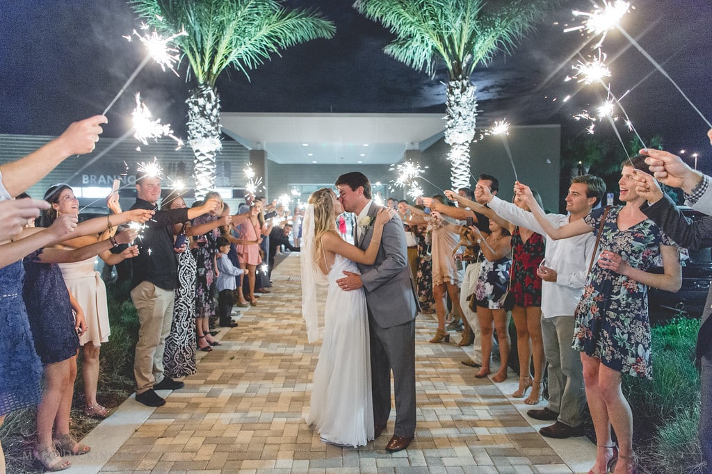 bride and groom kissing on brick path while wedding guests hold sparklers outside brannon center in florida