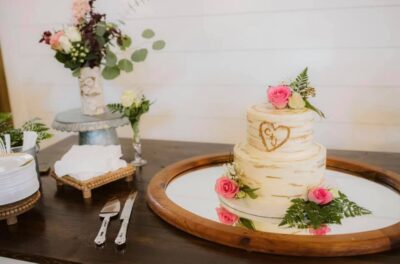 2 tiered cake with pink roses and initials carved into it like tree bark