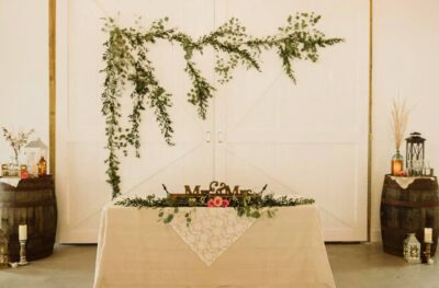 white table with green and pink floral garland with barrels decorated on either side and large green floral decor hanging on wall