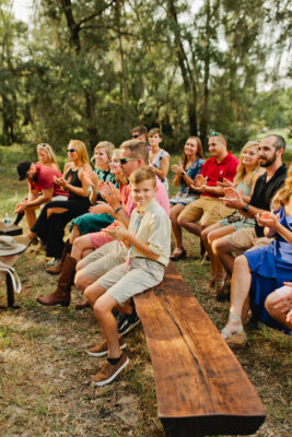 guests clapping during wedding ceremony while sitting on dark wood benches