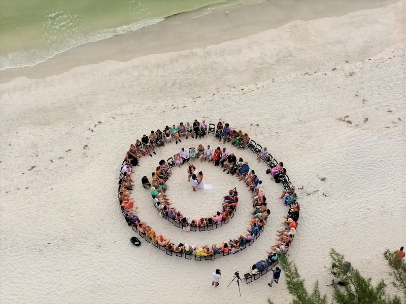 rented chairs arranged in a spiral formation on the beach with the bride and groom getting married in the center