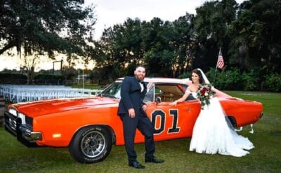 bride and groom leaning on orange sports car with number one on it