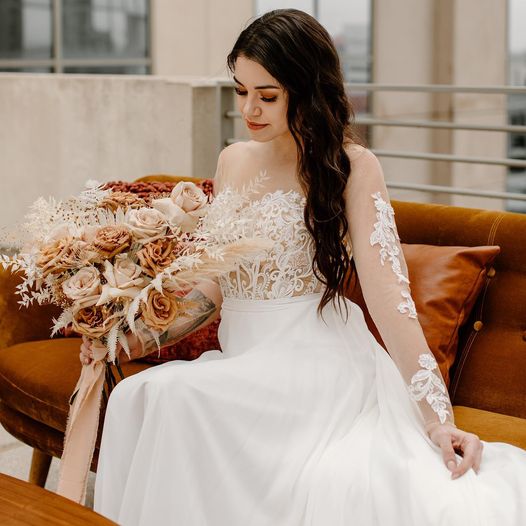 bride with hair and make-up by the Karmel Design Team in her wedding dress sitting on a couch holding her flower bouquet