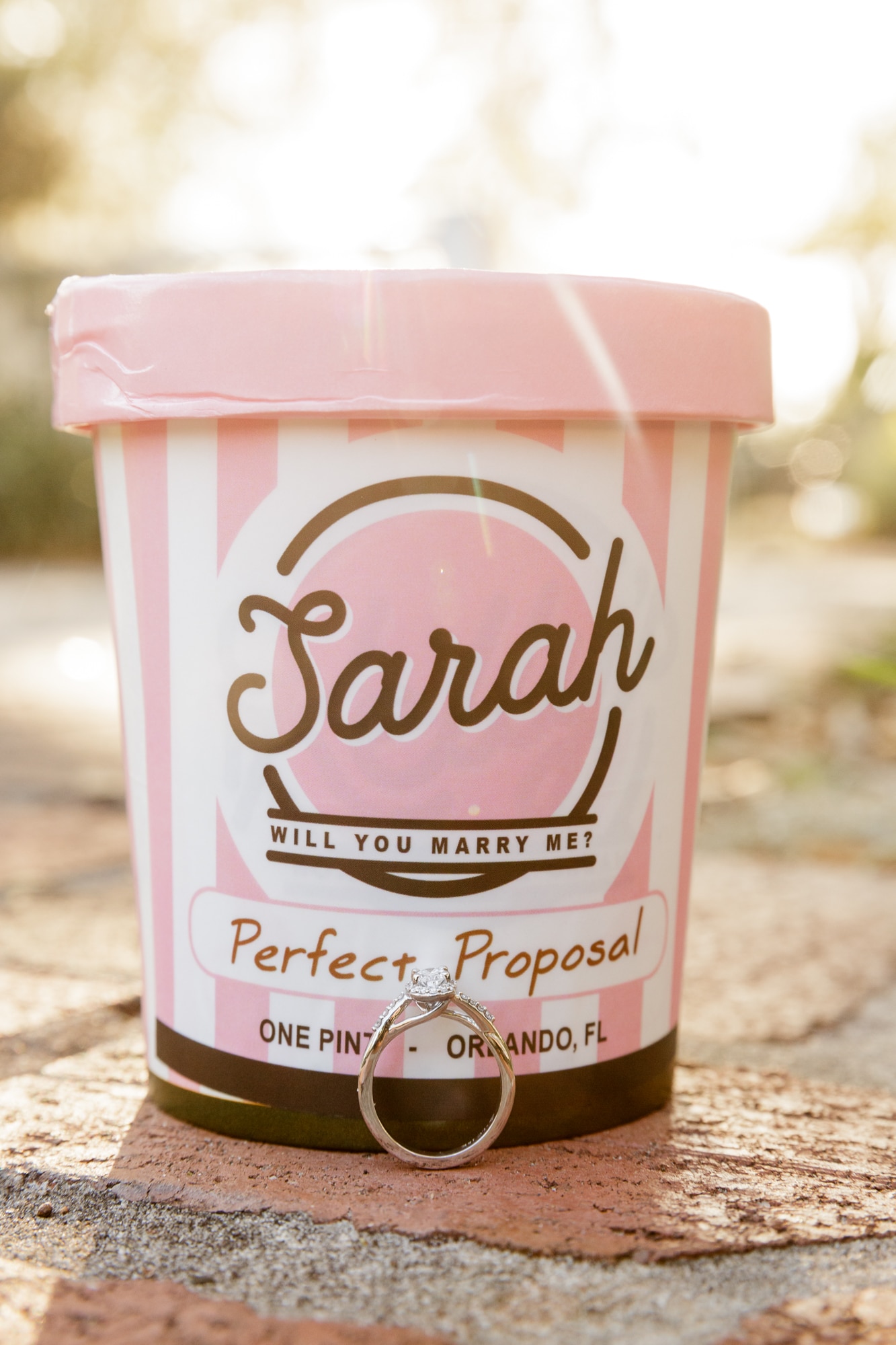 custom designed ice cream container with kelly's ice cream marriage proposal on it with engagement ring sitting in front of it on the brick paved ground