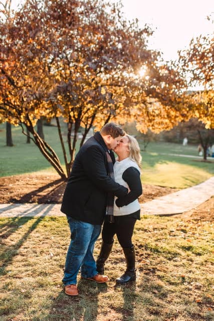 couple kissing in front of tree with golden autumn leaves on it