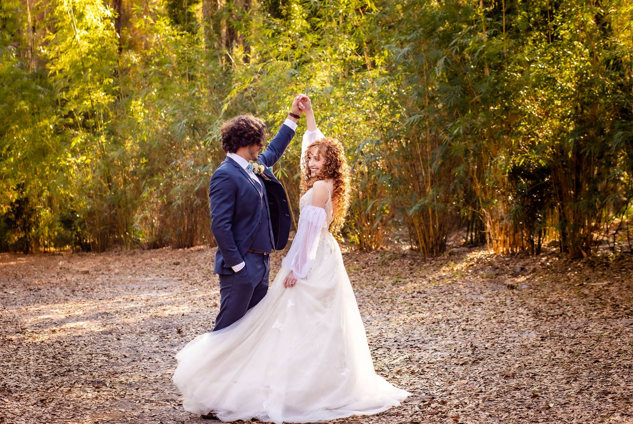 bride and groom outside surrounded by greenery with golden sunlight while groom spins bride around
