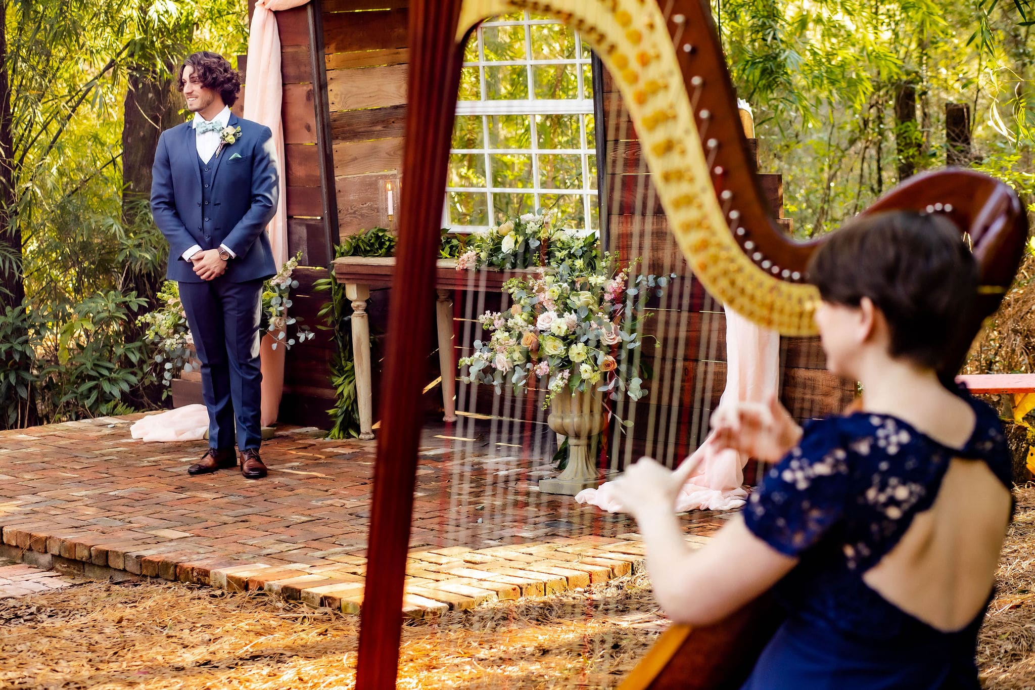 groom stands waiting at altar thats brick paved for bride as harpist plays off to the side