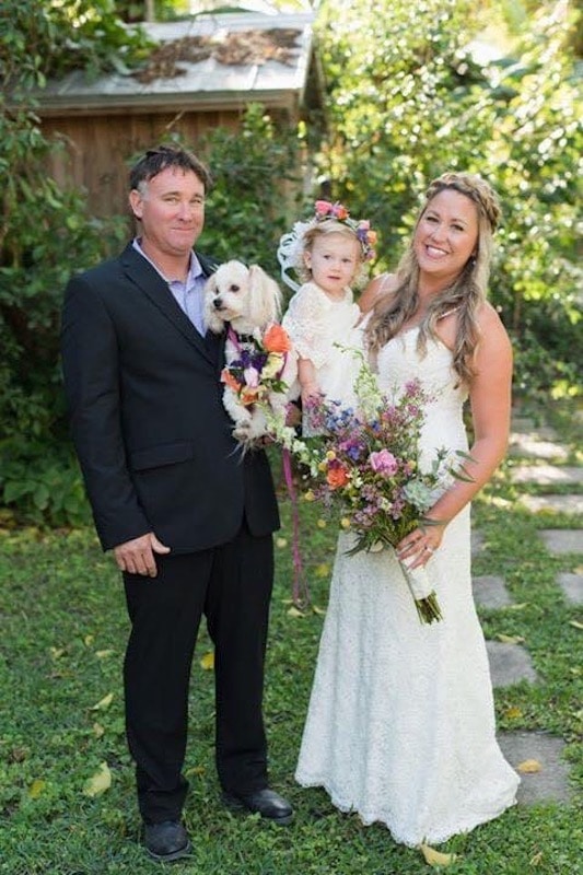 bride and groom holding their daughter and little dog on their wedding day