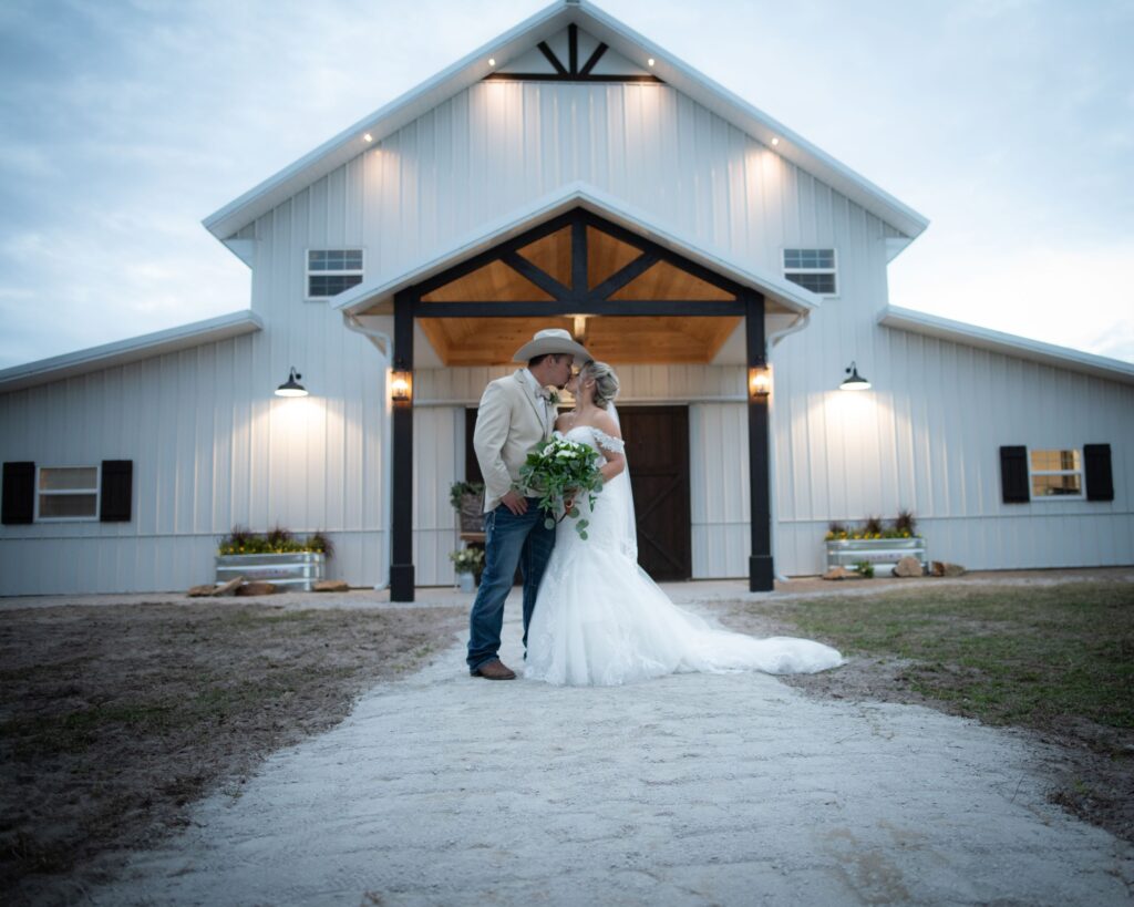 bride and groom kissing in front of large white barn