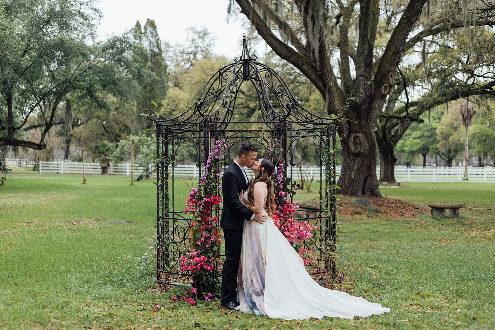 bride and groom kissing outside on their wedding day in front of steel frame gazebo