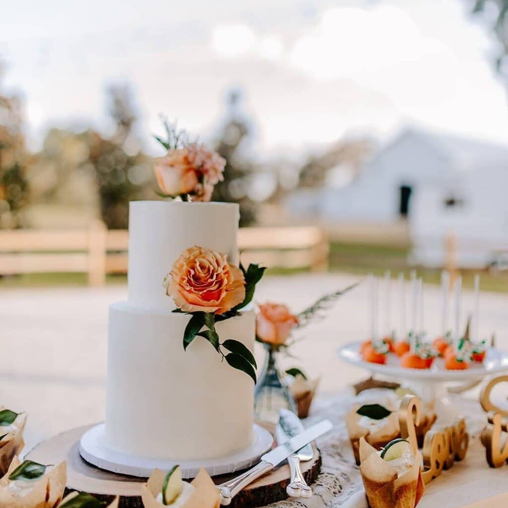 two tier white cake with orange roses in front of white barn