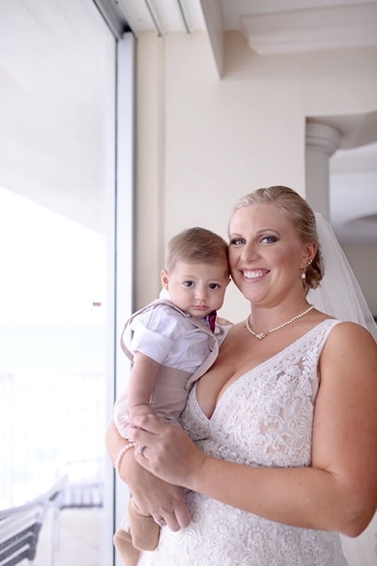 bride in her wedding dress with makeup from Blue Sky Beautify holding young boy