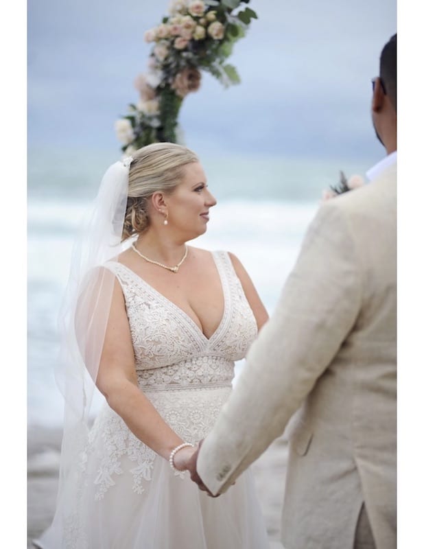 bride holding her grooms hands during wedding ceremony on the beach
