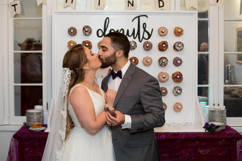 bride and groom kissing while standing in front of donut wall