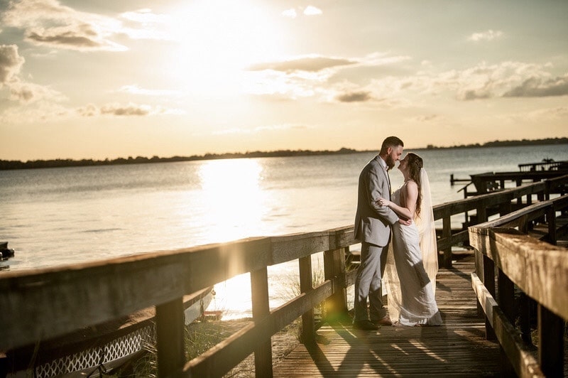 bride and groom standing on a dock at sunset