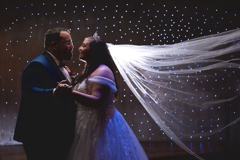 bride and groom dancing in the dark with little lights shining on the wall behind them and the bride's veil shining whtie