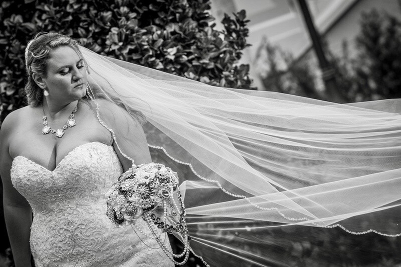 bride looking down at her flower bouquet as her veil floats in the wind next to her