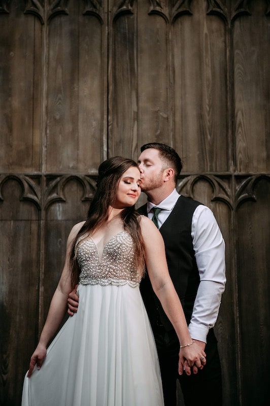 bride and groom kissing and holding hands while standing in front of large wooden doors
