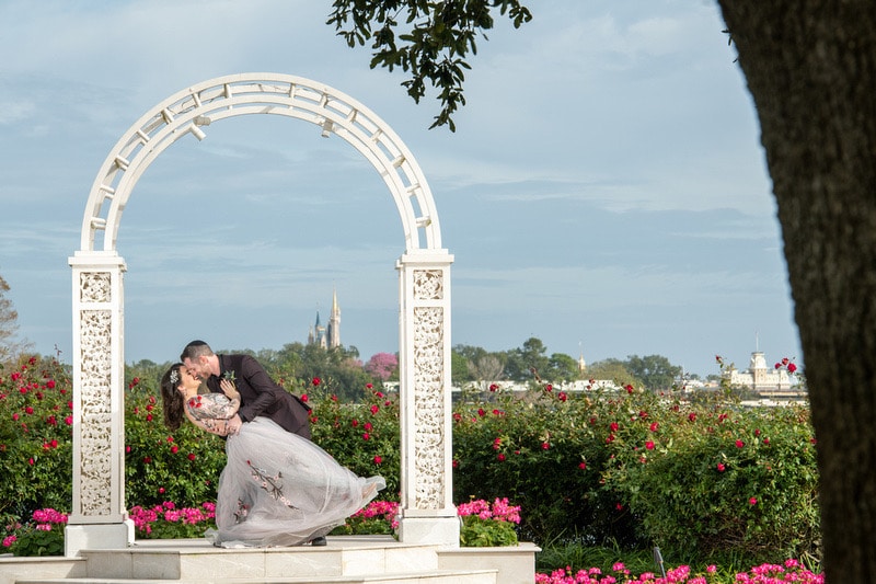 bride and groom kissing under an archway with Cinderella's castle behind them