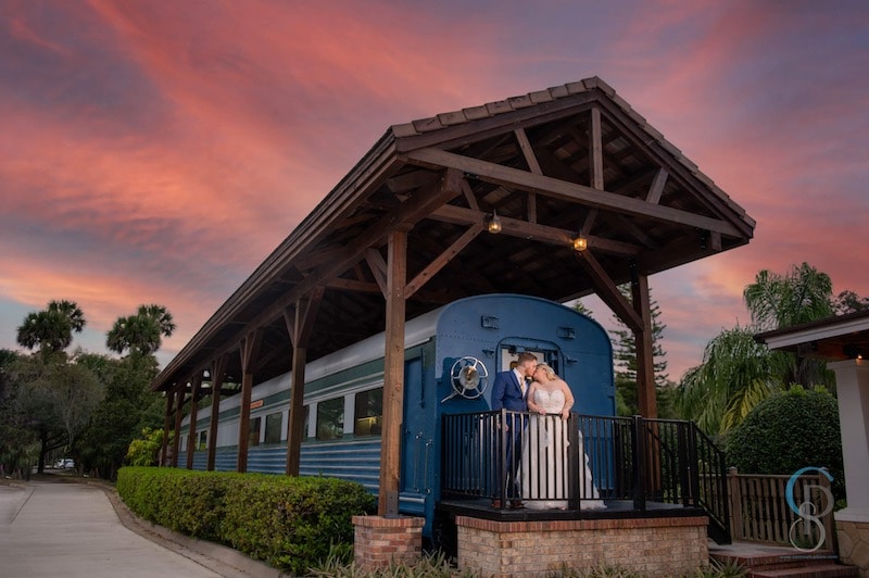 bride and groom kissing while standing on a platform with a blue train behind them