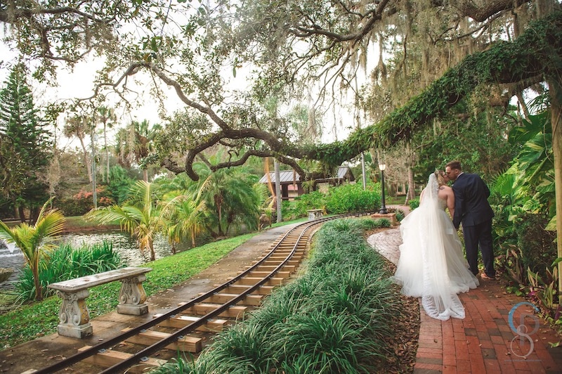 bride and groom kissing while walking through a lush garden landscape with train tracks cutting through
