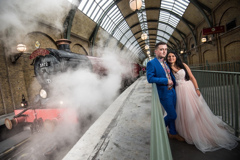 bride and groom leaning against the railing with steam from the Hogwarts Express train behind them