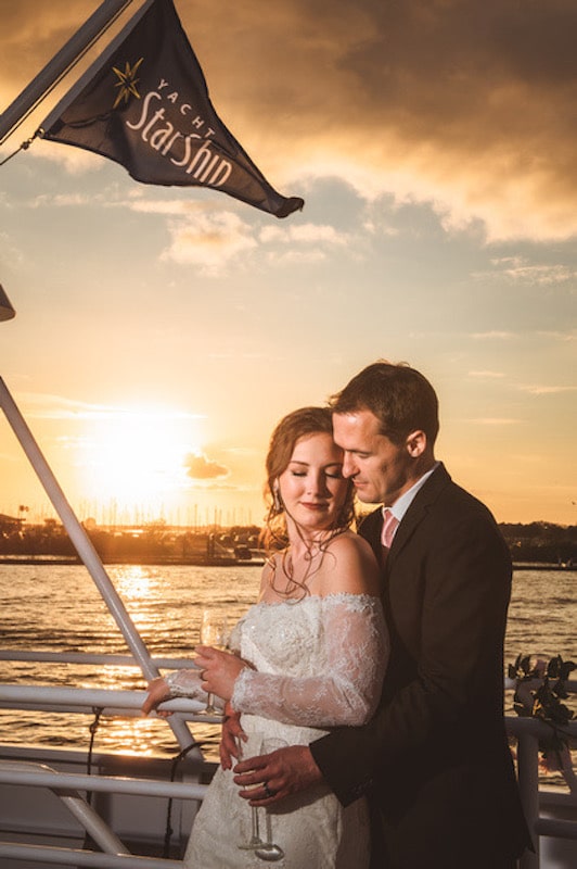 bride and groom embracing and drinking champagne on a yacht at sunset