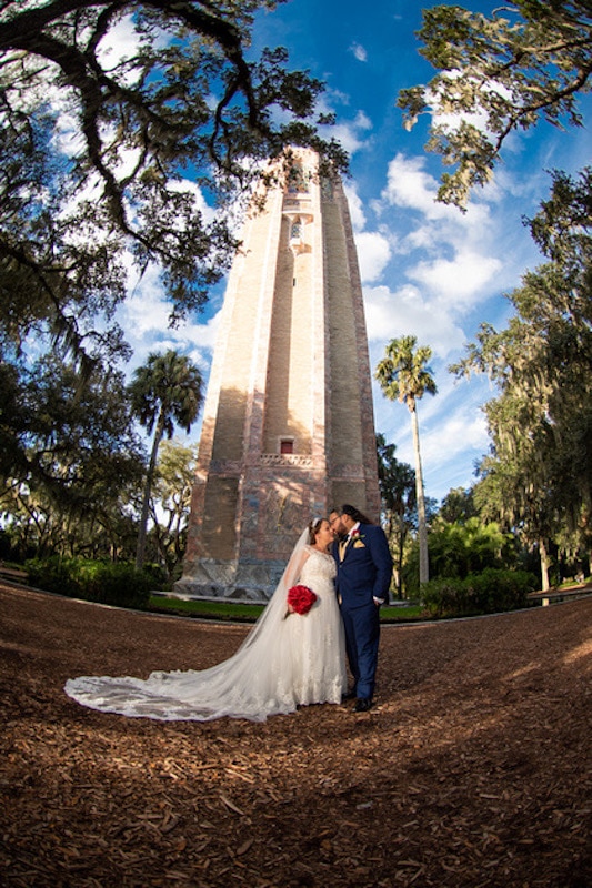 bride and groom kissing while standing underneath a monument