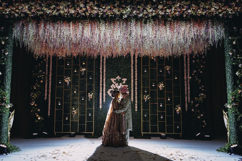 bride and groom embracing in front of wall made entirely out of plants and flowers, with pink flowers hanging from the ceiling