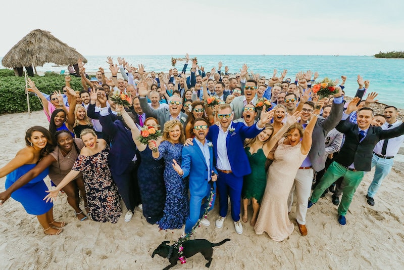 wedding party and guests cheering on beach overlooking ocean