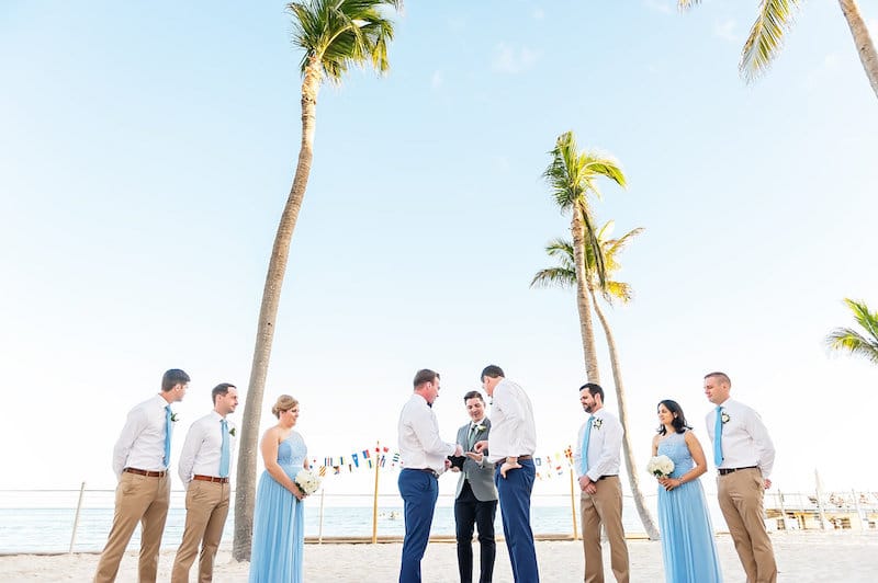 grooms grabbing the rings from the officiant during a beach wedding ceremony at event planned by Just Save the Date