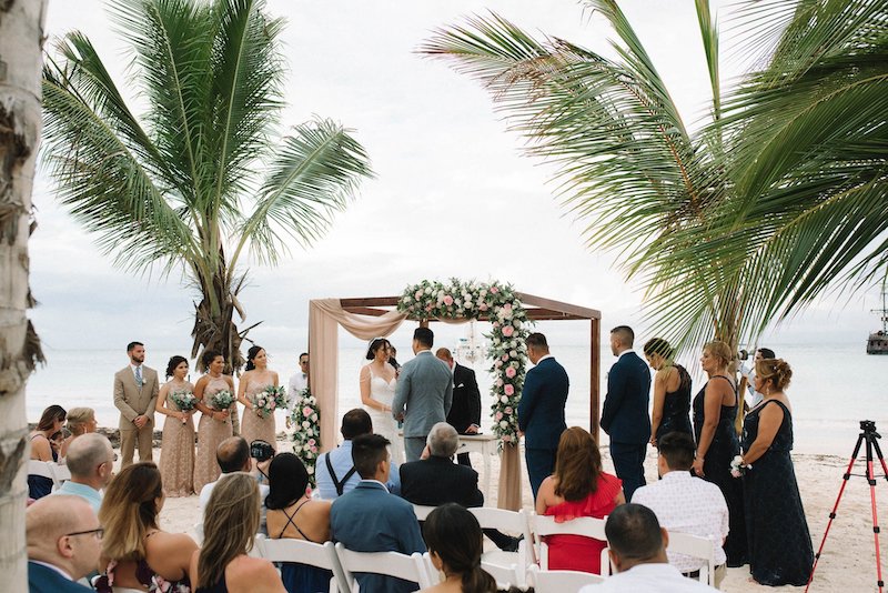 bride and groom exchange vows during beach wedding while guests look on
