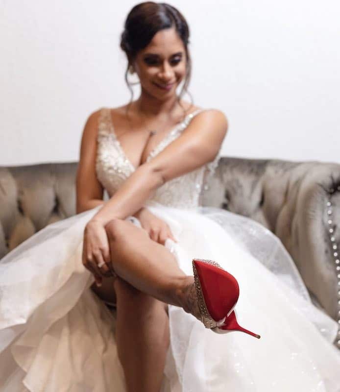 bride in her wedding dress sitting on a couch admiring her sparkly shoes