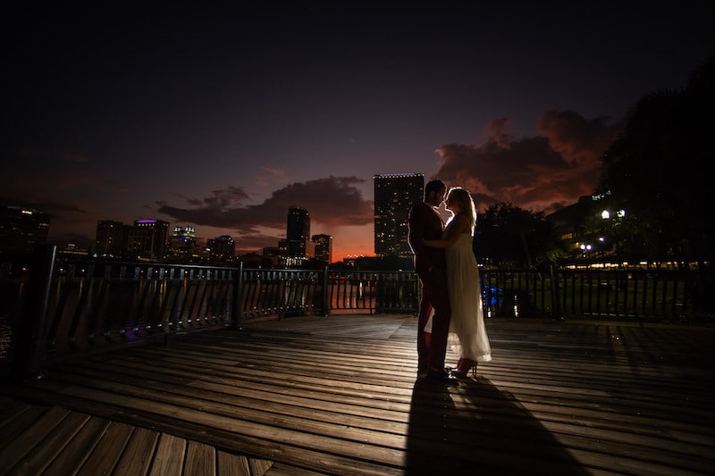 bride and groom hugging on boardwalk with night city skyline behind them